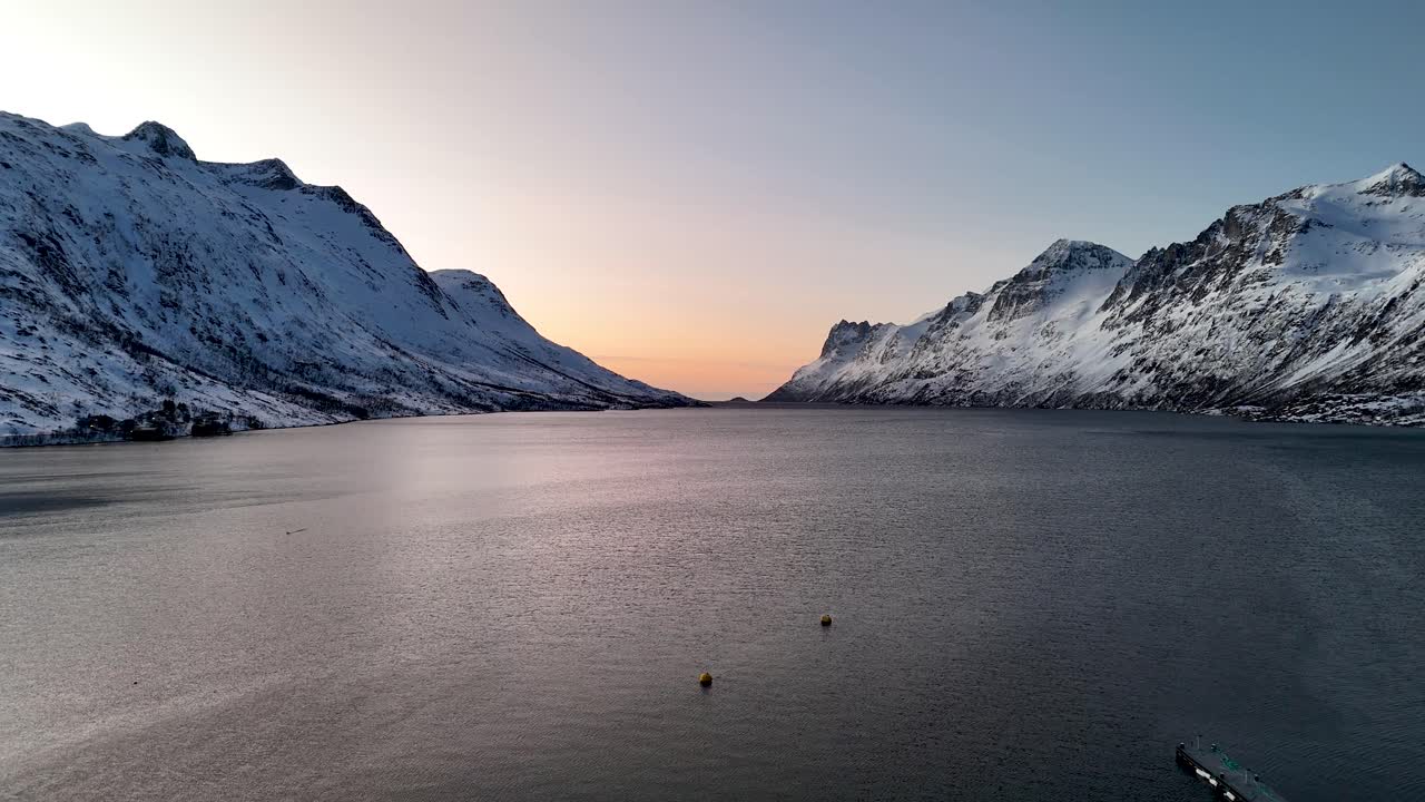 Ascensão vertical de drone sobre o fiorde de Ersfjordbotn na Noruega ao pôr do sol. Montanhas cobertas de neve cercam águas calmas do Ártico à luz de inverno de fevereiro