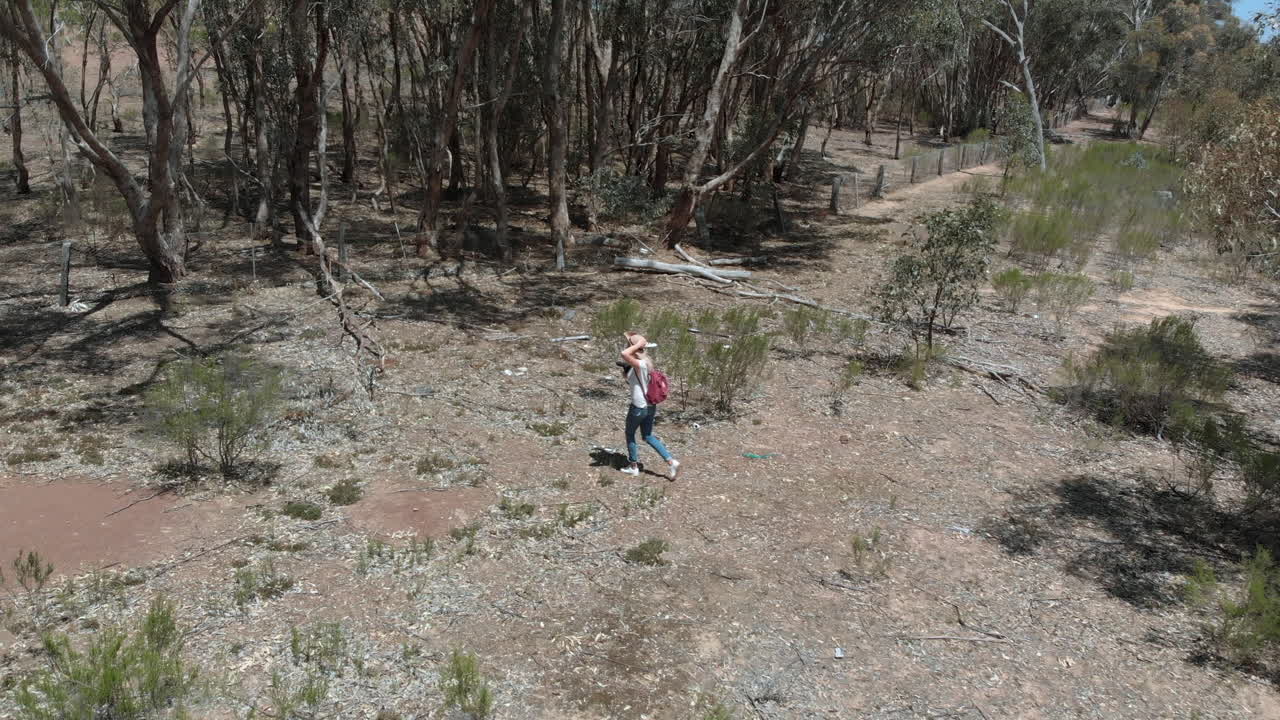 Close aerial following girl walking towards forest