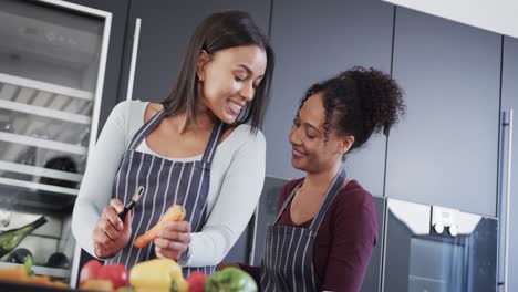 Happy-biracial-lesbian-couple-in-aprons-preparing-food-and-kissing-in-kitchen,-in-slow-motion