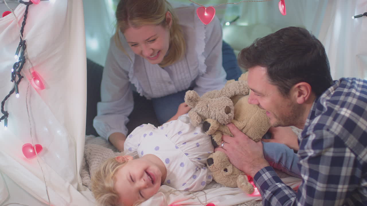 Laughing parents with young daughter having fun in homemade camp in child's bedroom at home - shot on slow motion
