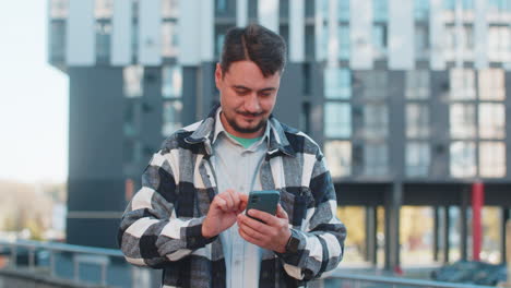 happy mature man tourist using smartphone and looking at camera while standing in downtown street