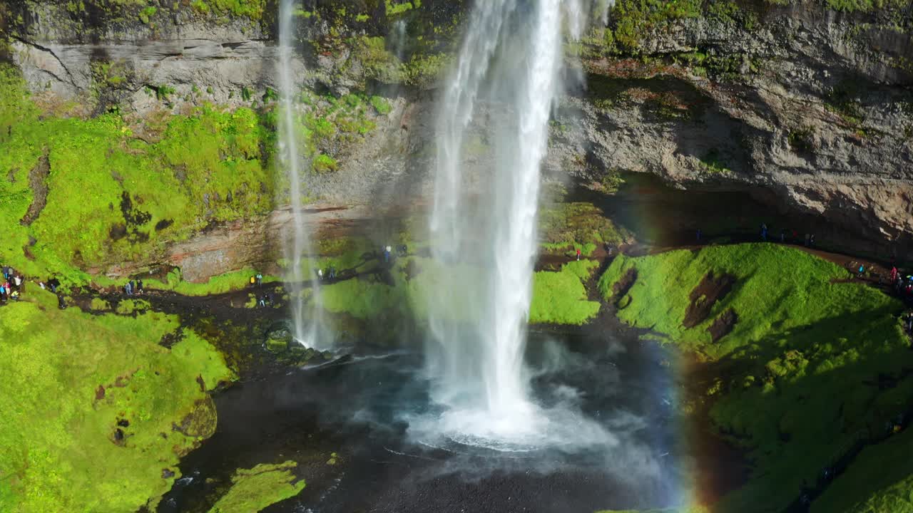 potente corriente de agua cayendo desde la cascada de seljalandsfoss con turistas paseando en verano en islandia - aéreo