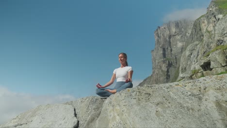 fit woman meditating on rocky coast, view from below and ascends