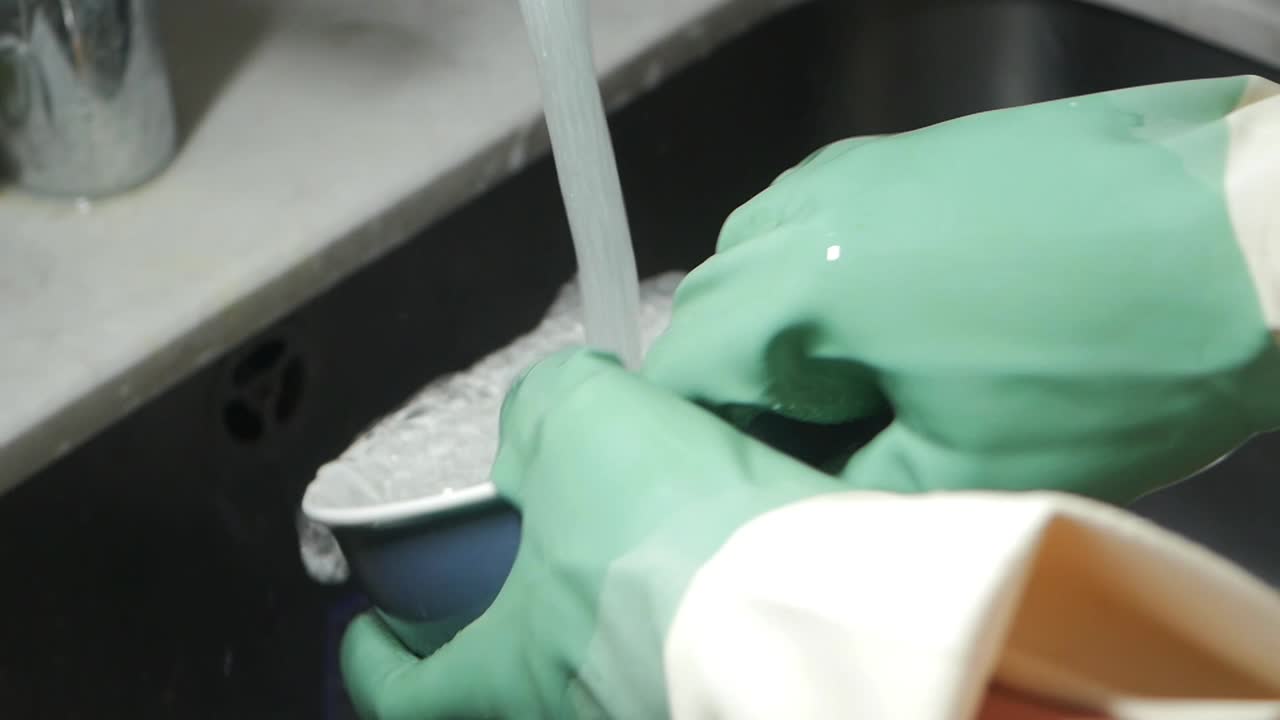 Hands in Green Gloves Washing a Bowl Under Running Water
