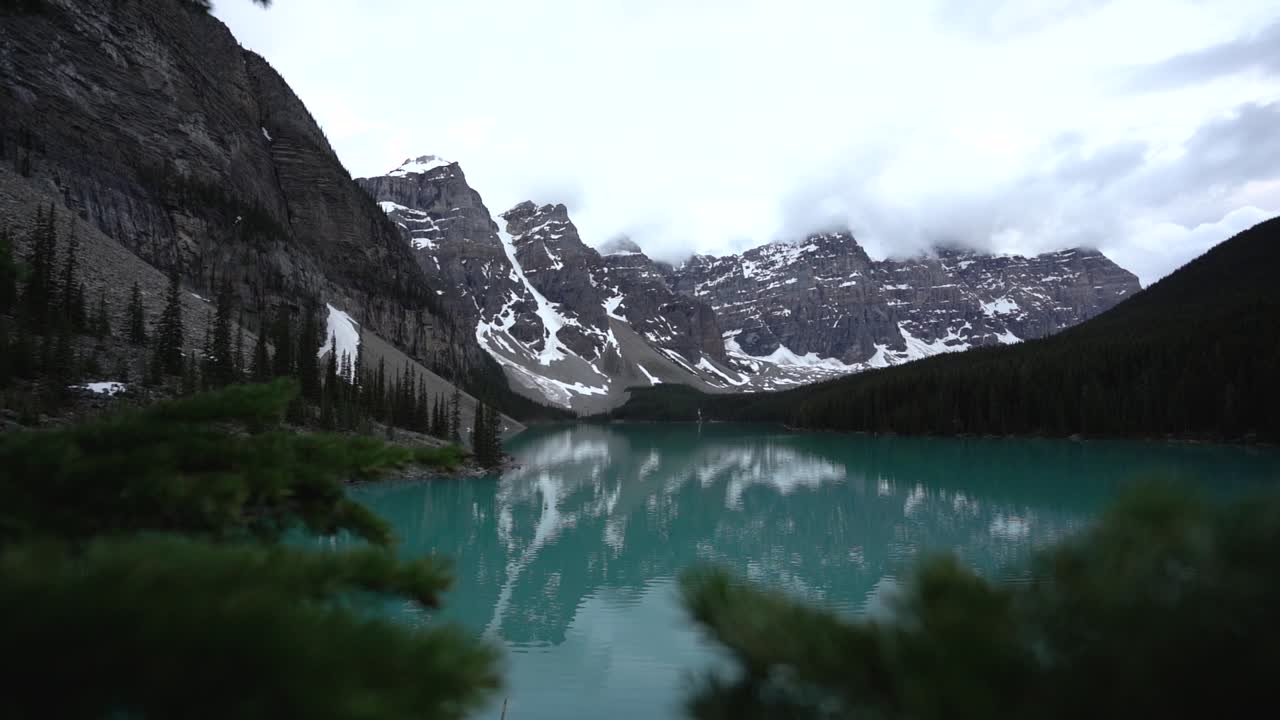 pan en cámara lenta de la morrena del lago con picos nevados detrás y nubes bajas
