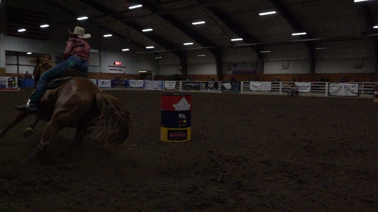 Cowgirl sur un cheval réalisant une course de barils dans un espace intérieur