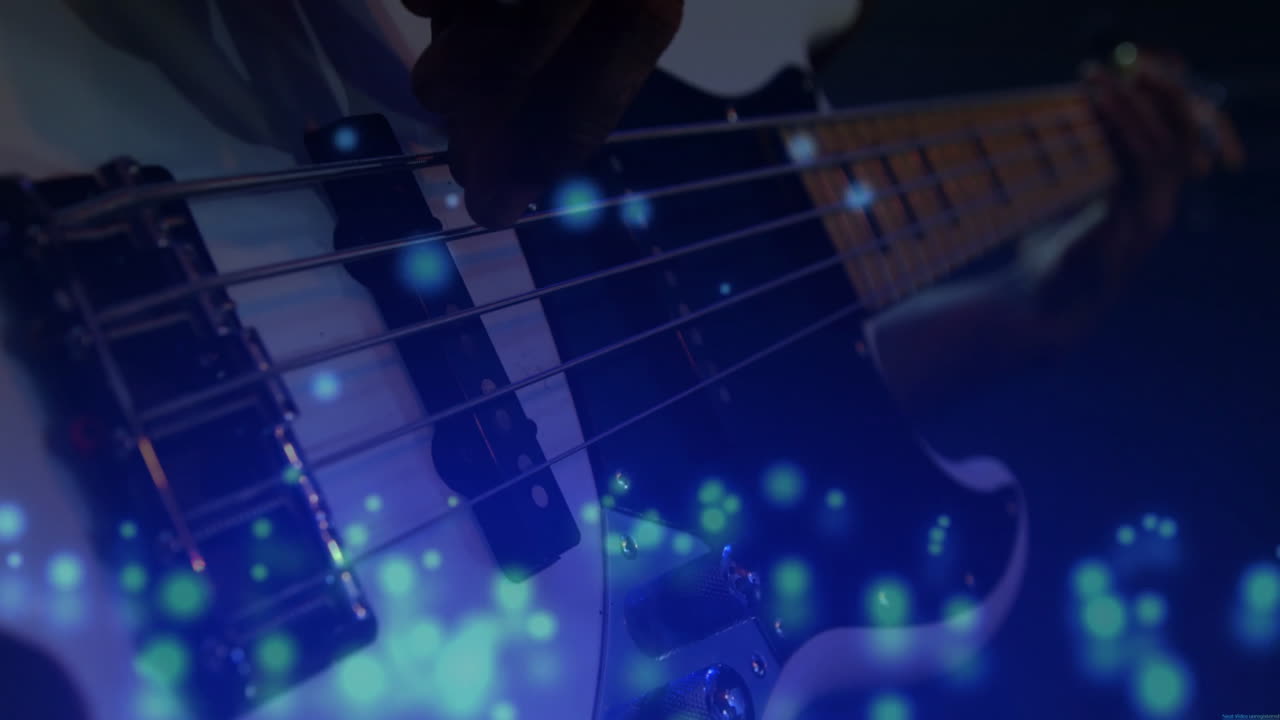 Musician's hand pressing bass guitar strings in music production, floating blue bokeh particles