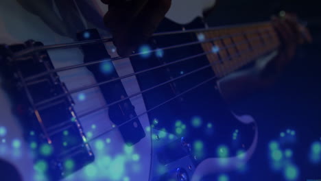 musician's hand pressing bass guitar strings in music production, floating blue bokeh particles