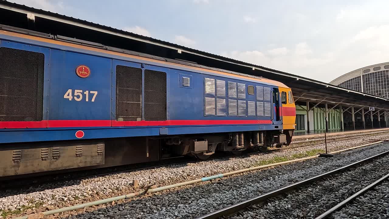 Side view of blue diesel locomotive slowly passing station platforms under soft afternoon daylight