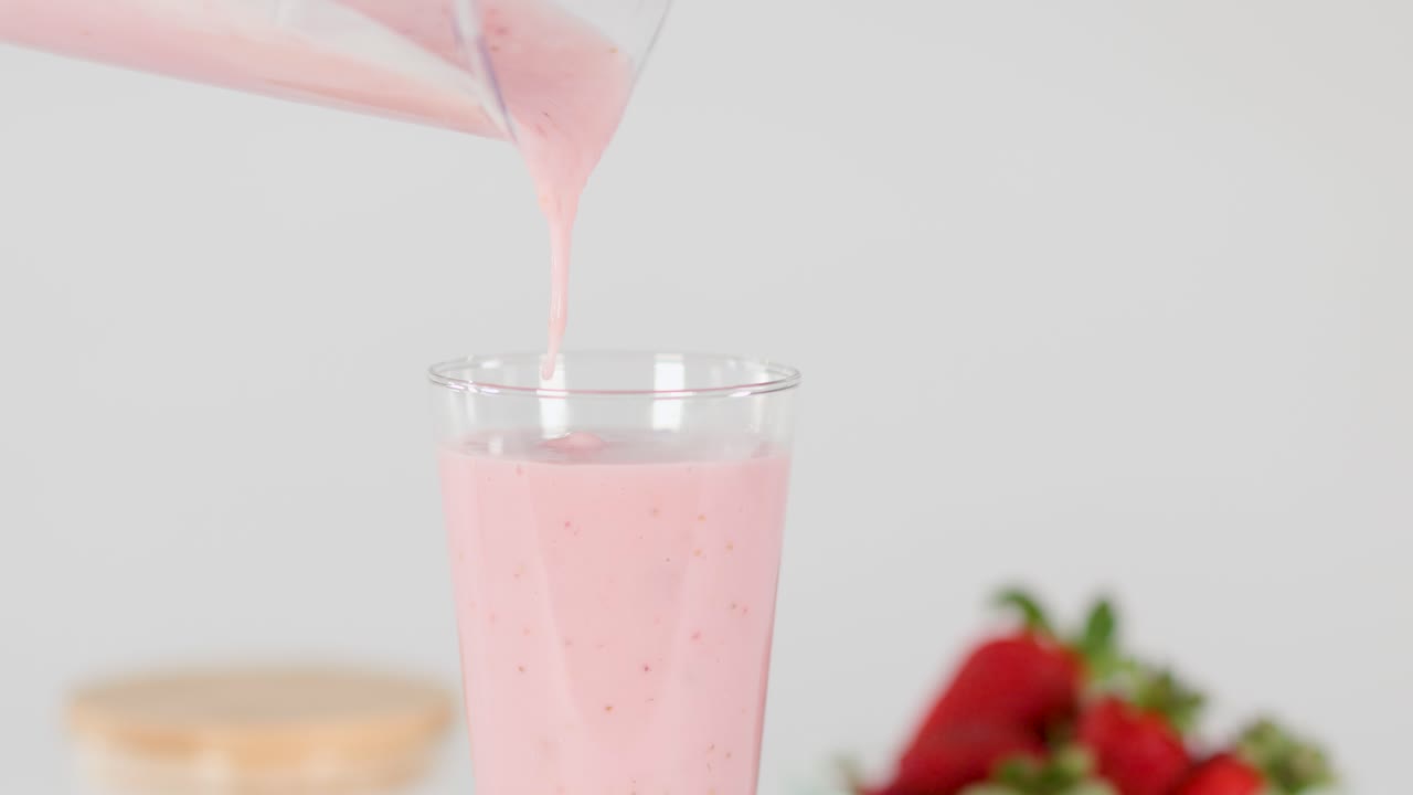 Fresh strawberry milkshake poured into glass, bright lighting, clean background, close-up, slow motion