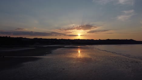 Sunset-rays-beam-fiery-golden-colours-across-relaxing-beach-ocean-coastline-aerial-view-right-dolly-slow-low