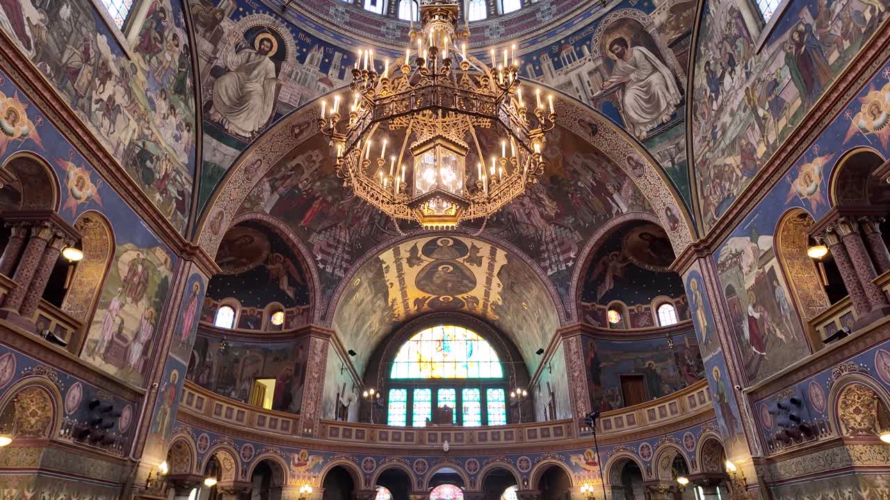Colorful ceiling frescoes, religious wall art, and illuminated chandelier in the Holy Trinity Cathedral of Sibiu, Romania