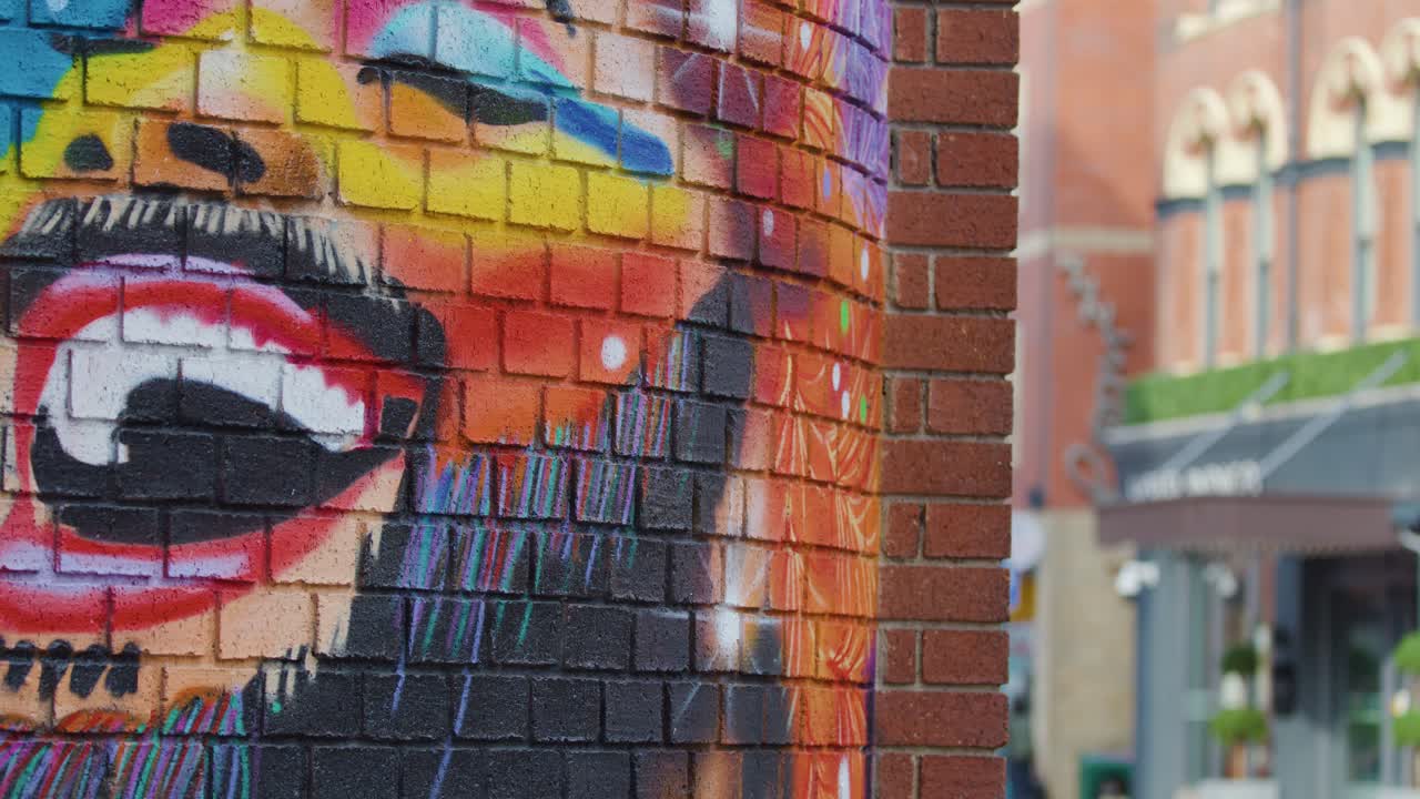 Camera pans from vibrant rainbow mural to urban street scene in daylight, highlighting public art