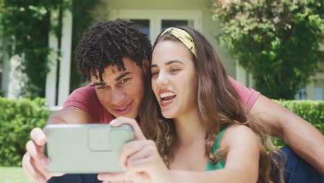 feliz pareja biracial pasando tiempo en el jardín y tomando selfies con el teléfono inteligente