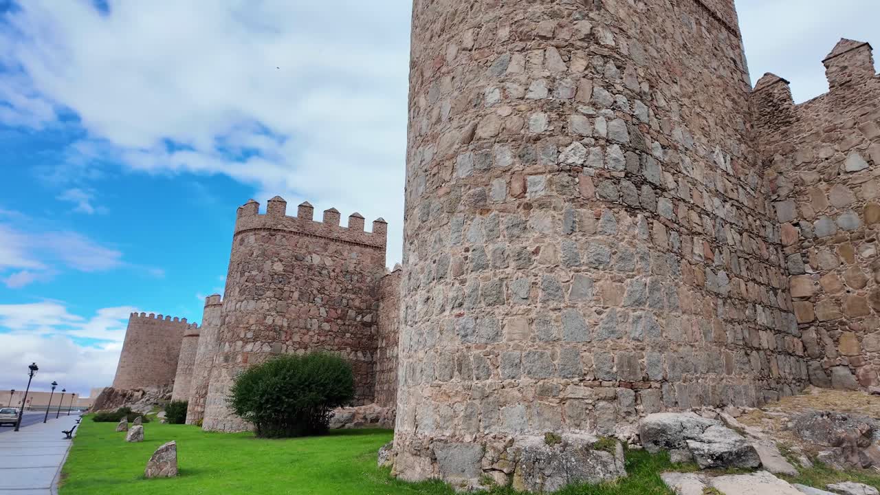 Ampia veduta delle storiche mura medievali di Ávila, Spagna, che si estendono su una collina erbosa sotto un cielo nuvoloso e drammatico, una delle città fortificate meglio conservate d'Europa e un sito patrimonio UNESCO