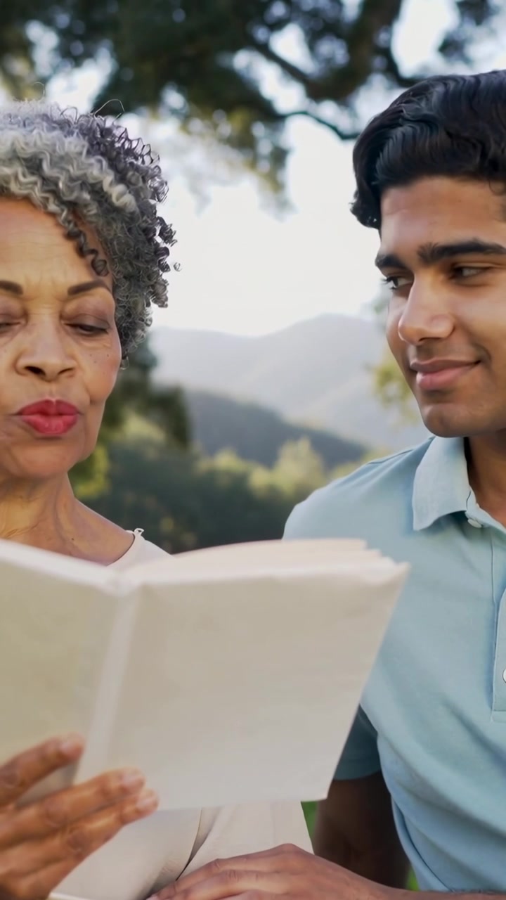 Vertical video: Lifting book, senior reading aloud in park, man in polo with binder sharing story