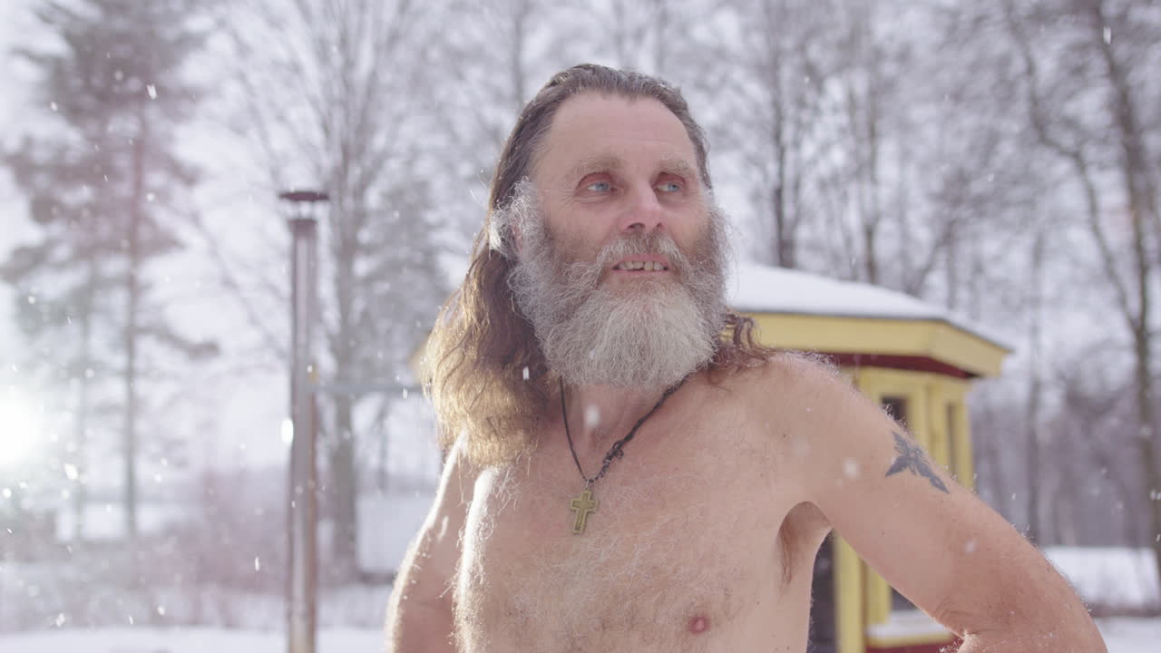 Contemplative hippy man stands bare chested in snowfall, looks skyward in prayer
