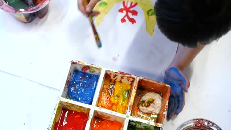 overhead shot of child dipping paintbrush into paint pallet to get blue paint for painting cute designs onto large sheet of white paper filmed in slow motion