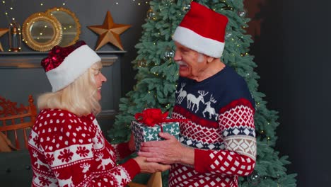 abuela mayor presentando una caja de regalo de navidad a un abuelo sorprendido en una habitación decorada