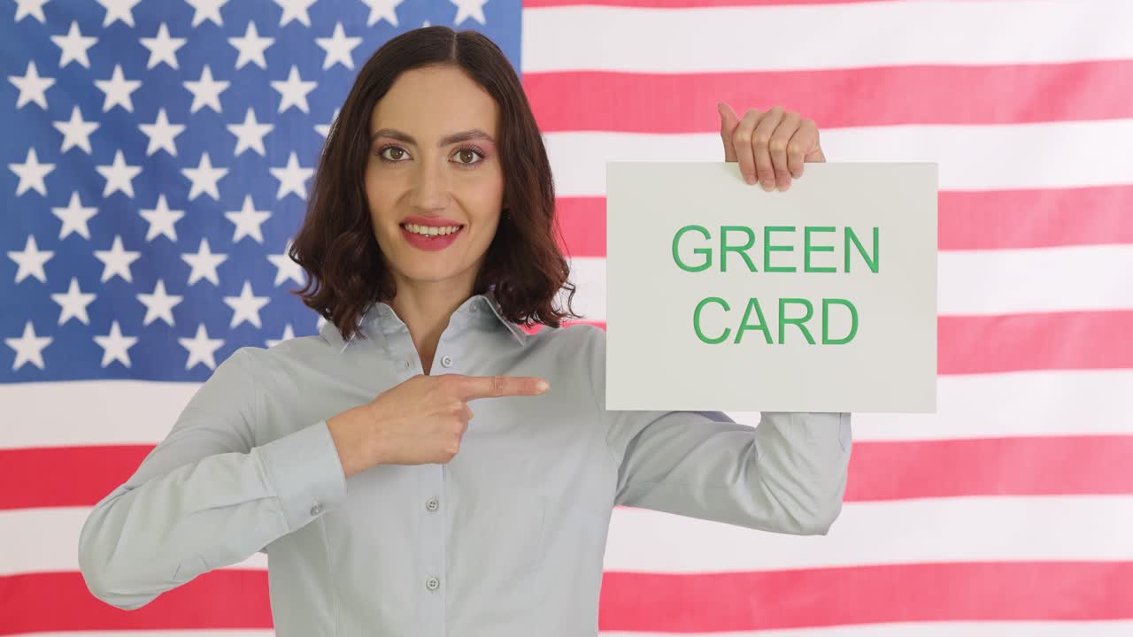 Woman holding a "Green Card" sign in front of the American flag