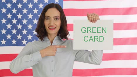 woman holding a "green card" sign in front of the american flag