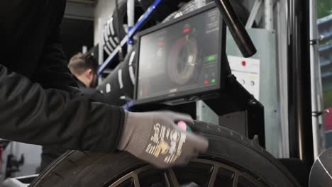 Tire-workshop-technician-using-auto-wheel-balancer-machine-to-analyze-wheel