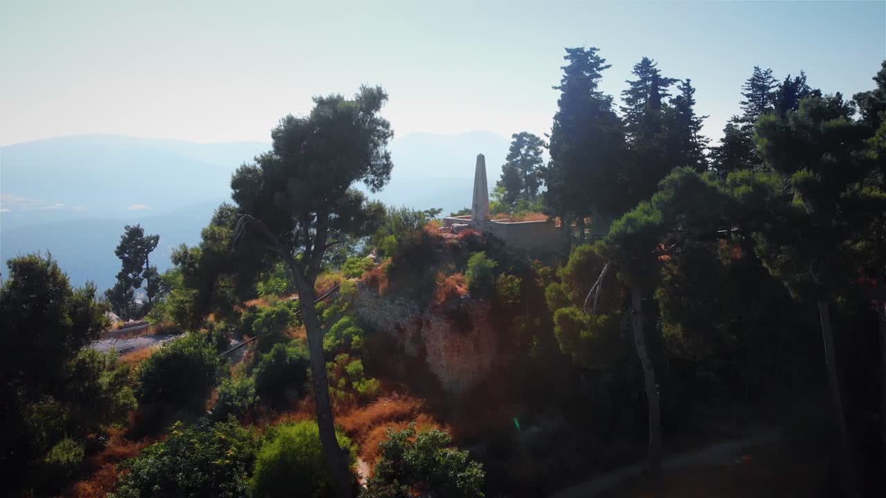 Obelisk monument on a tree-covered hilltop with a scenic mountain view