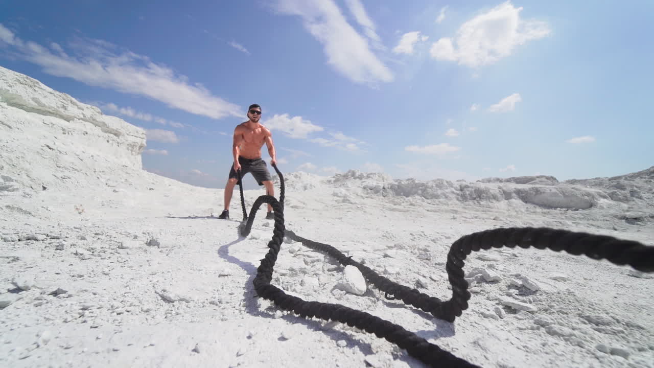 Bodybuilder exercising with battling ropes. Athletic young man working out with battle ropes on nature