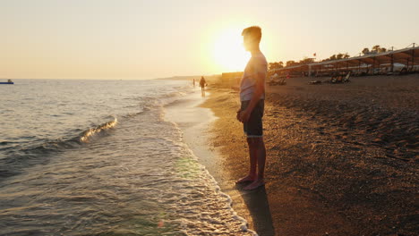 Junger-Mann-Steht-Am-Strand-Und-Bewundert-Den-Sonnenuntergang