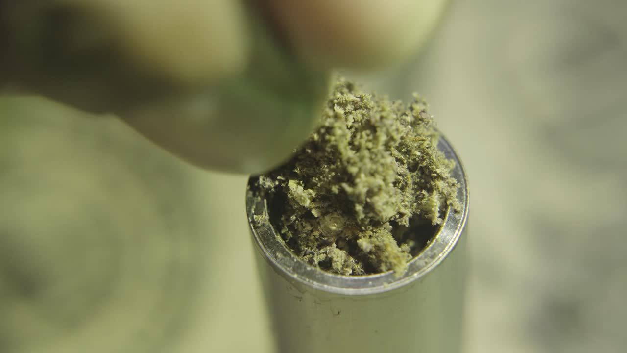 Extreme close-up of a hand packing ground herb into a vape pen chamber. Detailed, tactile motion.