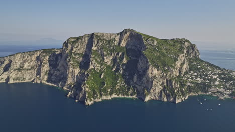 Capri-Italy-Aerial-v1-high-altitude-panning-shot-capturing-the-entire-island-town-in-a-coastal-landscape,-surrounded-by-deep-blue-sea-against-a-cloudless-blue-sky---Shot-with-Mavic-3-Cine---May-2023