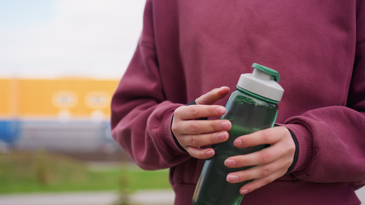 Closeup hand view of woman holding blue can against blurred urban backdrop outdoors with casual grip on bottle conveying hydration break during stroll in modern city environment scene