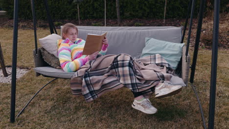 teenage girl reading in a garden swing