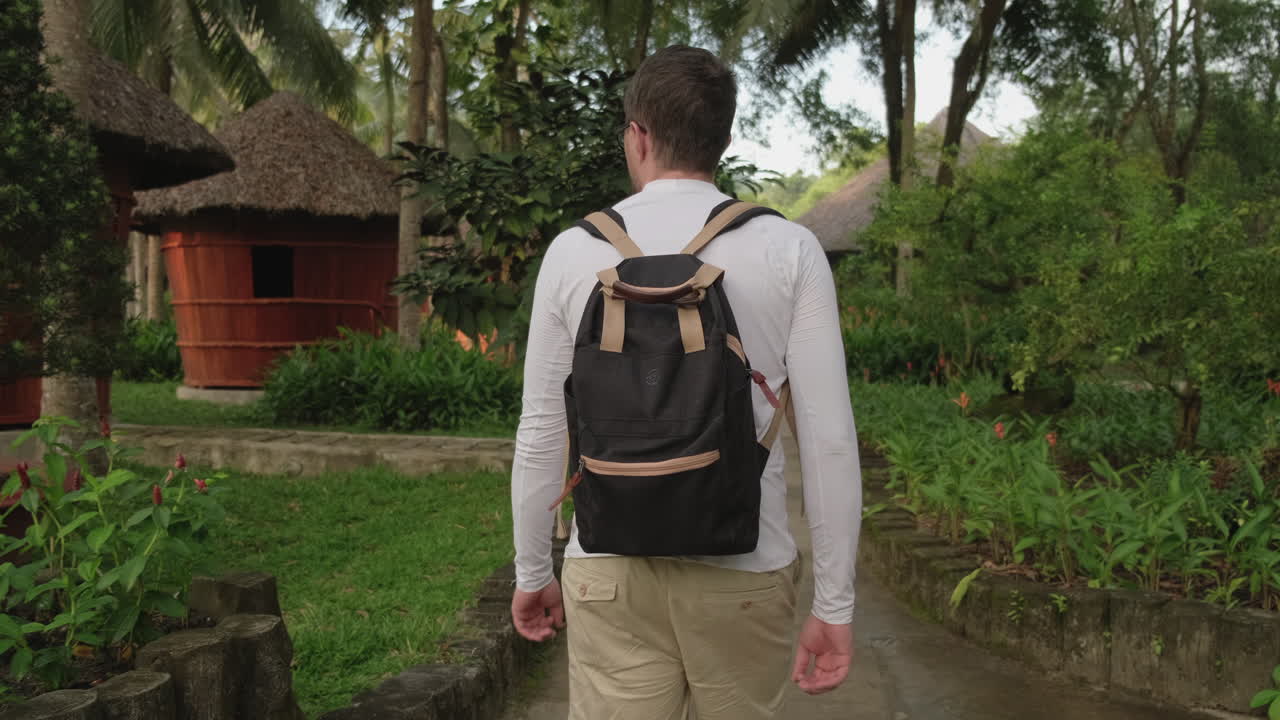 hombre caminando por un jardín tropical con cabañas