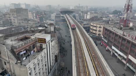 Luftaufnahme-Des-U-Bahn-Zugs-Der-Orangefarbenen-Linie,-Der-Sich-Dem-Bahnhof-In-Der-Nähe-Der-Mcleod-Road-In-Lahore-Auf-Einer-Erhöhten-Strecke-Nähert