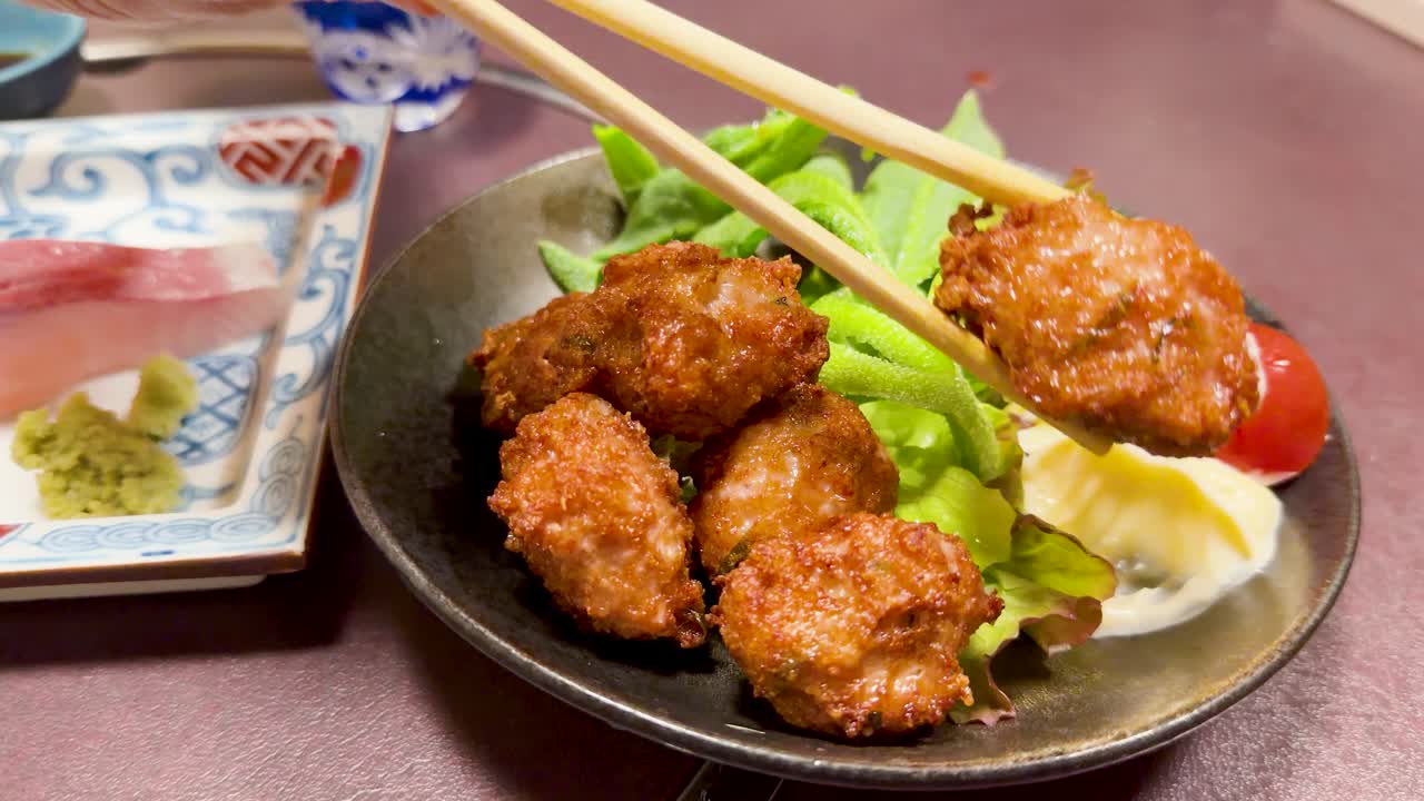 Крупный план: палочки для еды поднимают жареную куриную фрикадельку с тарелки с салатом