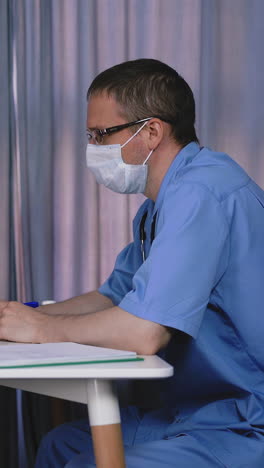 doctor, on face with mask and glasses, patient child comes, little girl, sits down, puts on table medical card, they laugh
