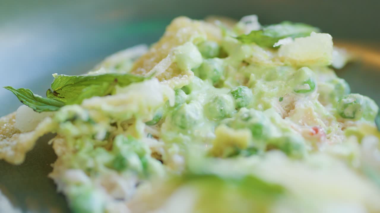 Close-up of a fork slicing into a fine dining crab cake topped with green peas and herbs, under soft natural lighting with shallow depth of field