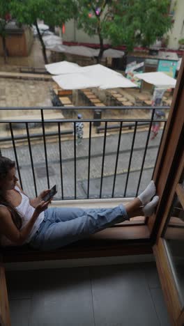 woman sitting on a balcony, looking at her phone on a rainy day