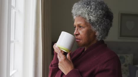 senior african american woman drinking coffee and looking out of the window at home