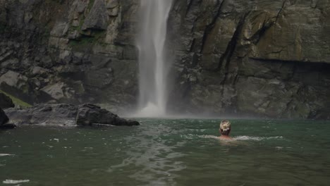 woman swimming in fresh water tropical pool with waterfall splashing