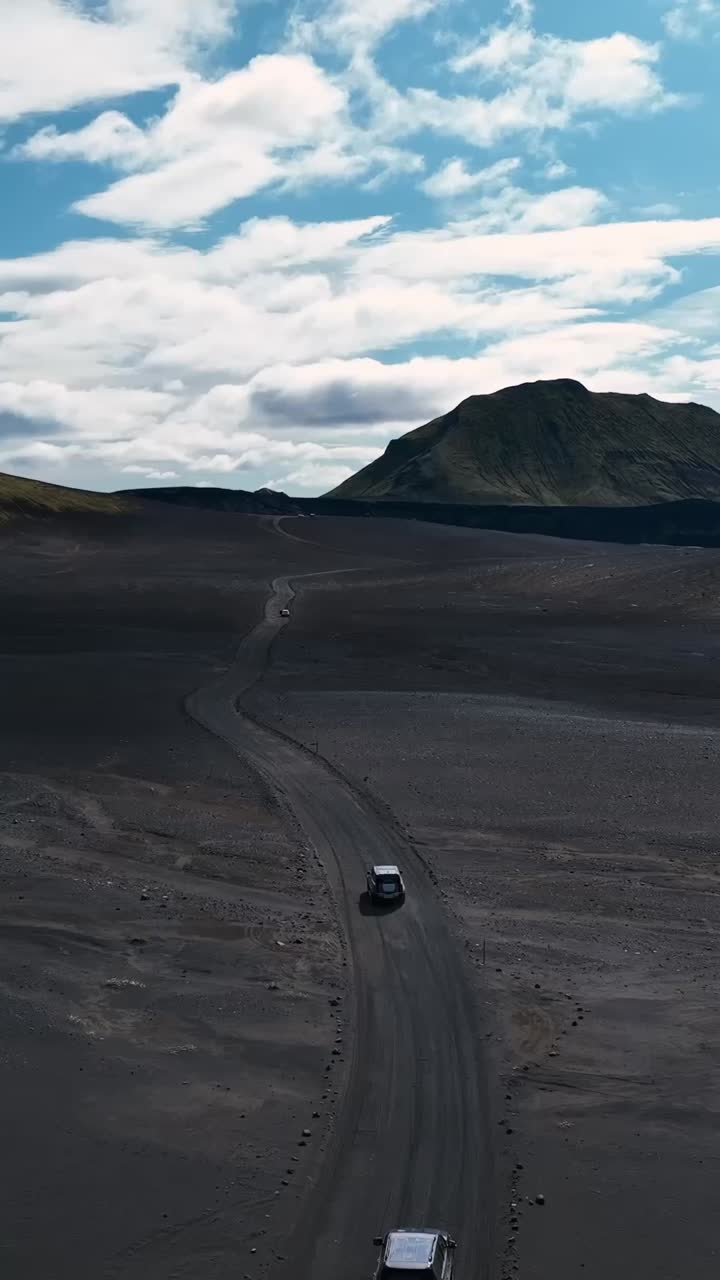 Clip verticale con drone di auto SUV che percorrono una strada sabbiosa e buia in Islanda con ripresa cinematografica.