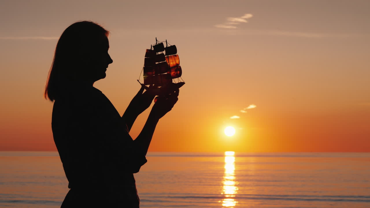 Una donna con una barca in mano si trova in riva al mare dove il sole tramonta. Concetto di creatività e ispirazione