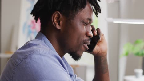 Close-up-of-stressed-african-american-male-artist-talking-on-smartphone-at-art-studio