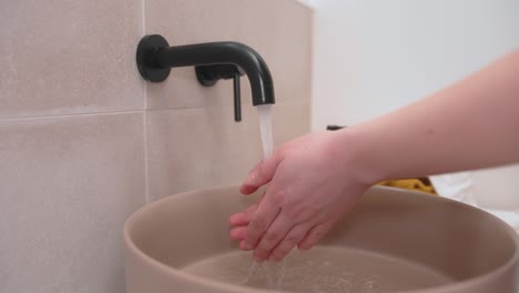 Woman-washing-her-hands-under-bathroom-tap