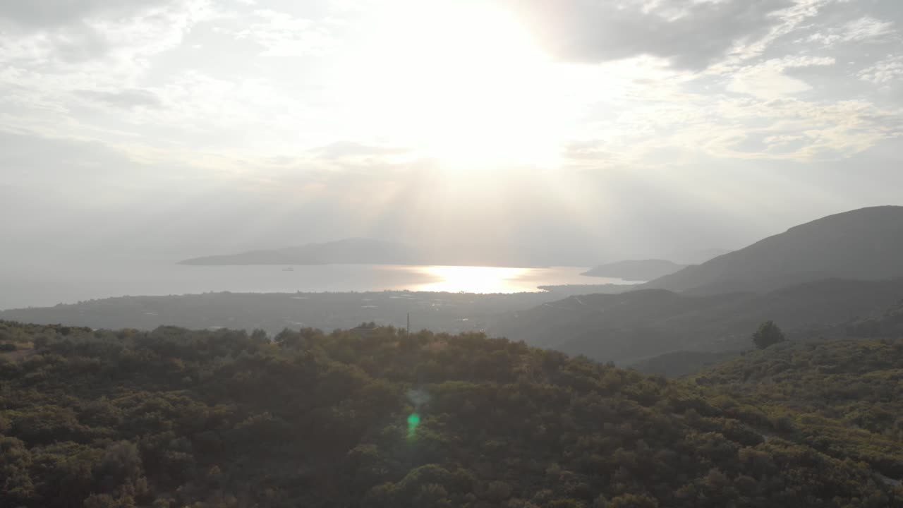 aerial  day drone shot of amazing mountain landscape  green tall trees small traditional village sun shines behind white clouds sun reflects in the sea at background amazing view