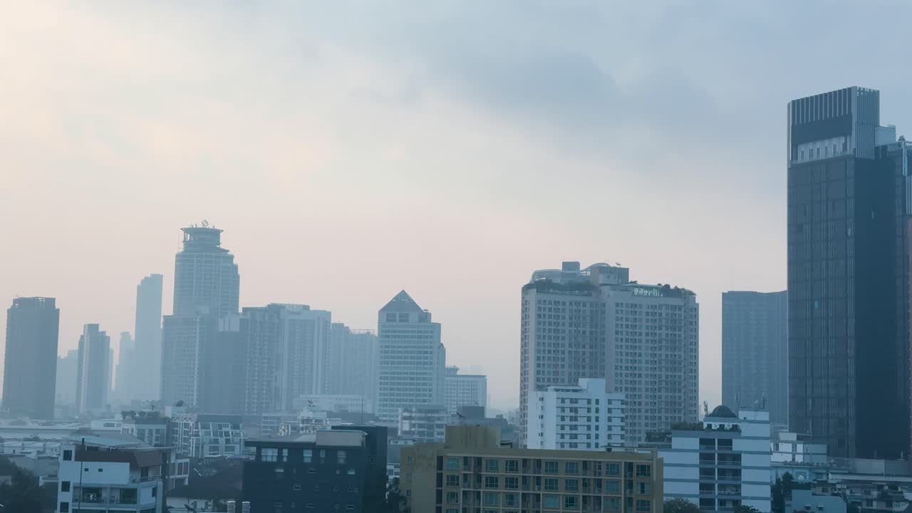 Plano estático amplo de arranha-céus em Bangkok obscurecidos por poluição densa sob um céu cinzento