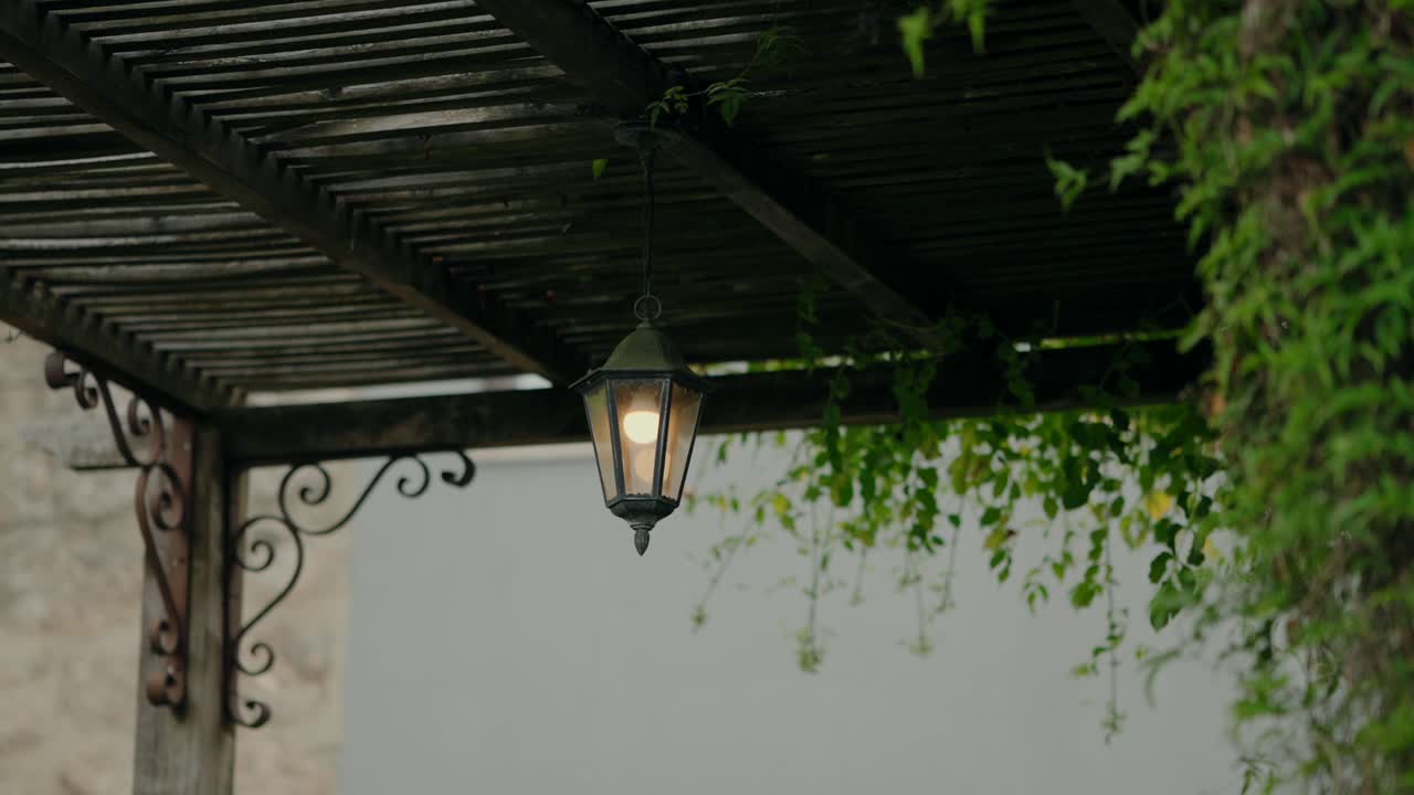 outdoor lantern hanging under a wooden pergola with ivy vines, softly lit in a peaceful setting