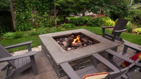 orbiting shot of a propane fire pit with a roaring flame surrounded by chairs on a patio during the day