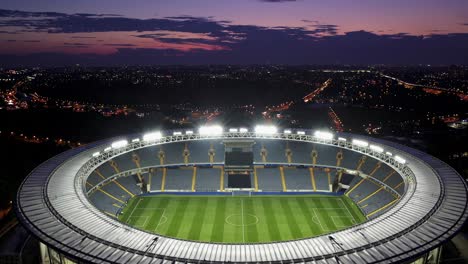 stadium lights illuminating urban landscape at dusk, revealing dramatic contrast between architectural design and city skyline during evening twilight